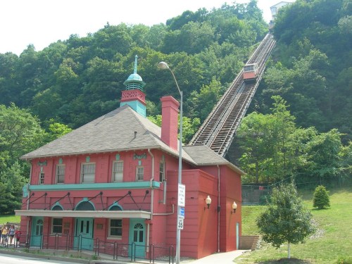 A colorful building at the base of a steep hill with a funicular railway ascending the slope.