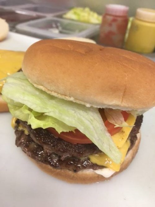 A close-up of a hamburger with lettuce, tomato, cheese, and a beef patty, served on a soft bun.