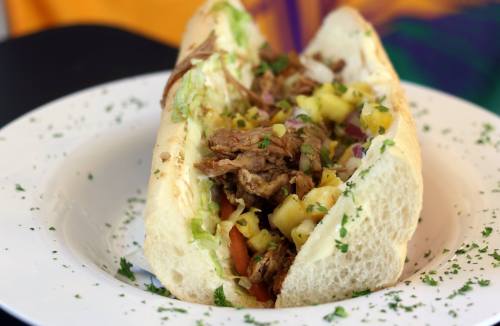 A close-up of a sandwich filled with shredded meat, lettuce, and pineapple salsa, served on a white plate.