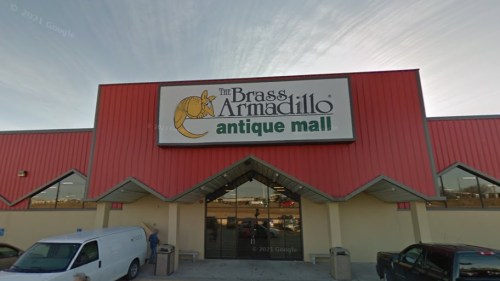 Exterior of The Brass Armadillo antique mall, featuring a large sign and a red building with a blue sky above.