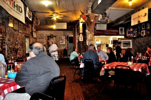 A cozy restaurant interior with checkered tablecloths, diners enjoying meals, and rustic decor on the walls.