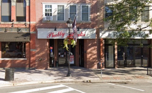 A brick building with a sign reading "Philly Jacks," featuring outdoor seating and decorative flowers.