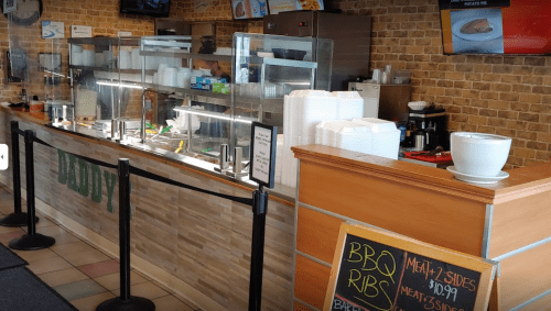 A BBQ restaurant counter with a menu board, display of food items, and a seating area in a cozy setting.