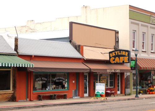 A quaint café with a sign reading "Skyline Café," featuring colorful awnings and a welcoming outdoor sign.
