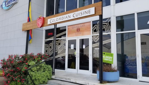 Exterior of a restaurant named "Colombian Cuisine" with a sign and open door, surrounded by greenery.