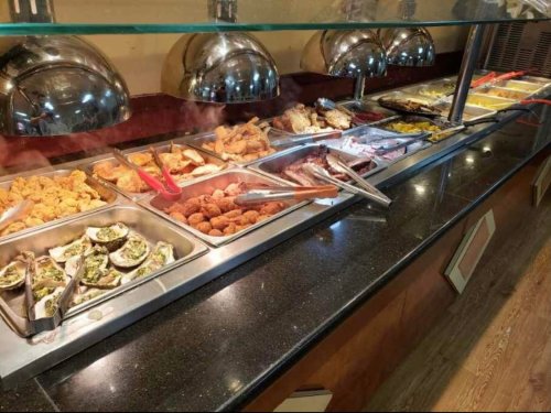 A buffet with various dishes, including fried chicken, seafood, and sides, displayed in metal trays under warming lights.
