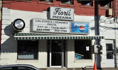 Exterior of Fiori's Pizzaria featuring a sign with menu items and a Pepsi logo, with a striped awning.