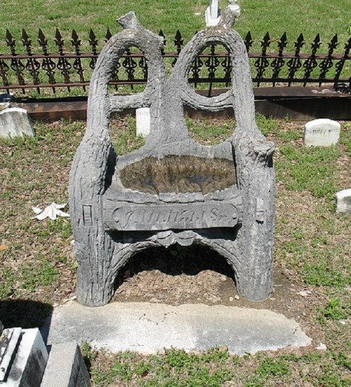A unique gravestone shaped like a tree bench, with intricate bark details, set in a grassy cemetery.