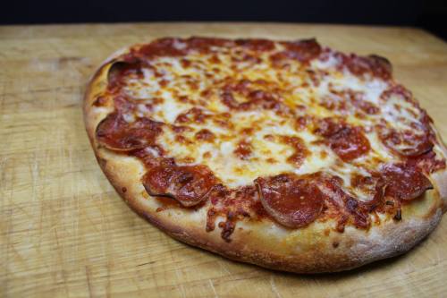 A freshly baked pepperoni pizza with melted cheese on a wooden cutting board.