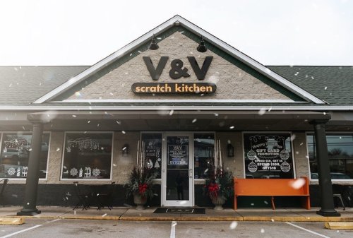 Exterior of V&V Scratch Kitchen with snow falling, featuring a welcoming entrance and festive decorations.