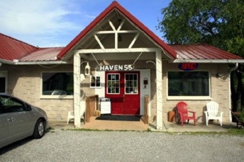 A quaint building with a red roof and open sign, featuring a welcoming entrance and outdoor seating.