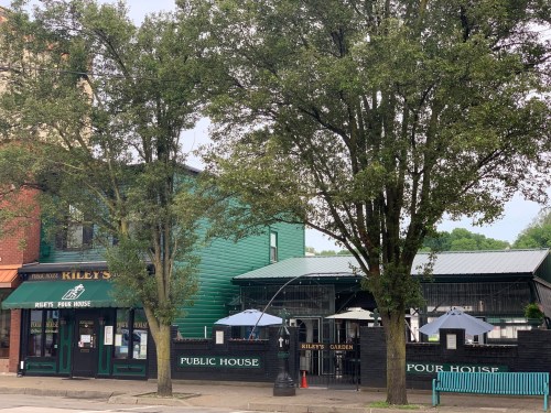 A green building with "Kiley's Pour House" signage, outdoor seating, and trees in front.