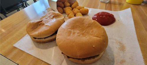 Two burgers on a paper tray with a side of tater tots and a small bowl of ketchup.