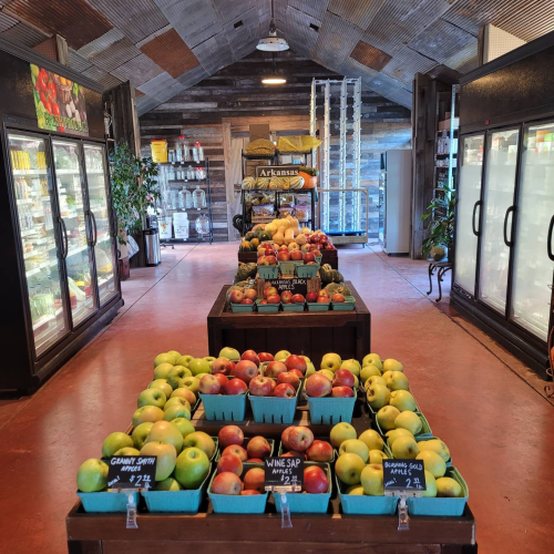 A rustic market interior with wooden displays of colorful apples and refrigerated sections in the background.