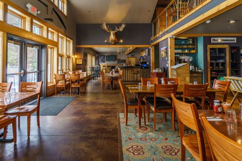 Interior of a cozy restaurant with wooden tables, chairs, and large windows, featuring a rustic decor and warm lighting.