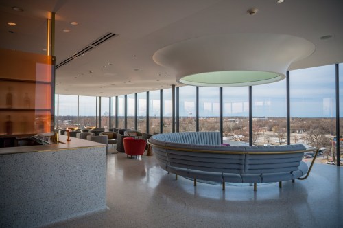 Modern interior of a bright lounge with large windows, featuring a curved sofa and stylish seating arrangements.