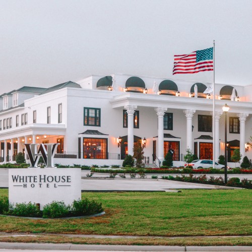 Exterior of the White House Hotel with an American flag and landscaped grounds.