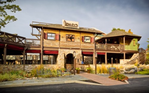 A rustic wooden restaurant with a stone facade, featuring outdoor seating and a welcoming entrance.