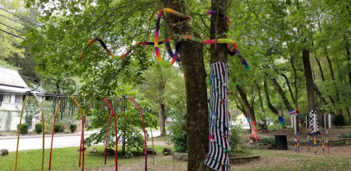 Colorful ribbons and fabric hang from trees in a park, creating a vibrant, artistic outdoor installation.