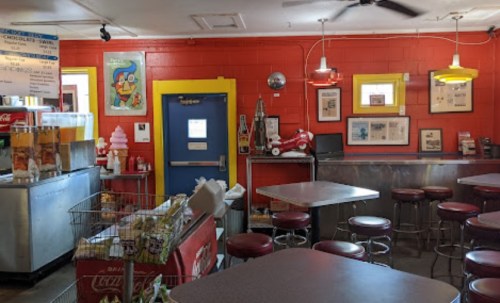 Colorful diner interior with red walls, yellow accents, metal tables, and vintage decor, featuring a snack display and ice cream machine.
