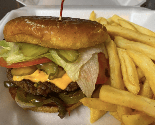 A juicy cheeseburger with lettuce, tomato, pickles, and onions, served with a side of golden French fries.