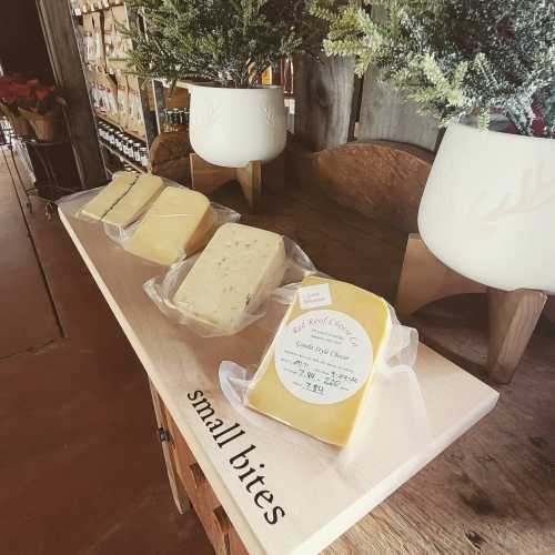 A wooden table displays four varieties of cheese, labeled "small bites," in a rustic shop setting.