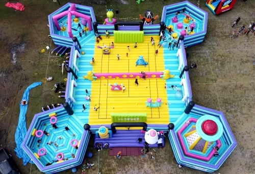 Aerial view of a colorful inflatable playground with various sections for jumping and playing, filled with people.