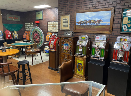 A vintage gaming room featuring slot machines, a roulette table, and horse racing artwork on brick walls.