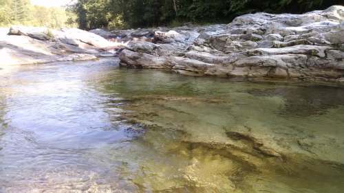 A serene river scene with clear water flowing over smooth rocks, surrounded by lush greenery.