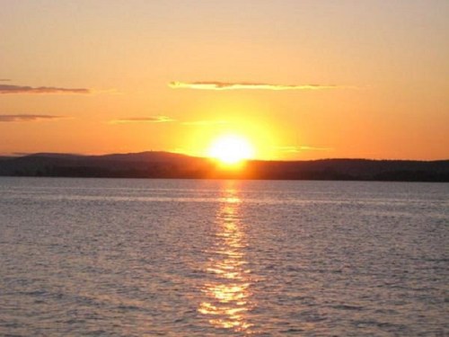 A serene sunset over calm waters, with vibrant orange and yellow hues reflecting on the surface.
