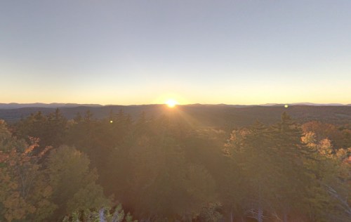 A serene sunset over a mountainous landscape, with trees in the foreground and a warm glow in the sky.