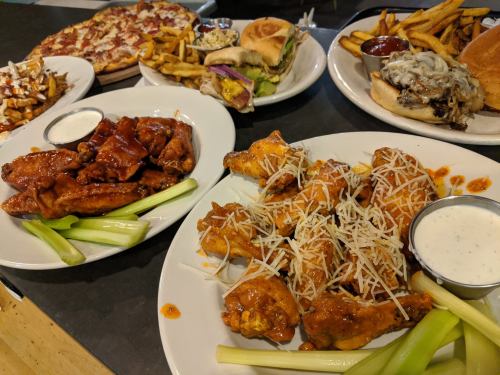 A spread of delicious food including wings, pizza, burgers, fries, and dipping sauces on a table.