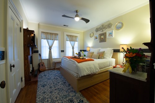 Cozy bedroom with a bed, decorative pillows, a guitar, and a vase of flowers, featuring warm lighting and soft colors.
