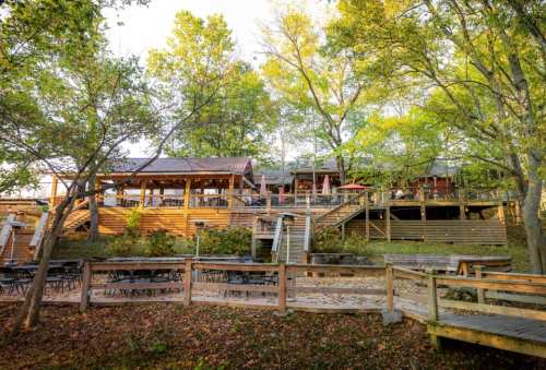 A rustic restaurant surrounded by trees, featuring outdoor seating and wooden walkways.