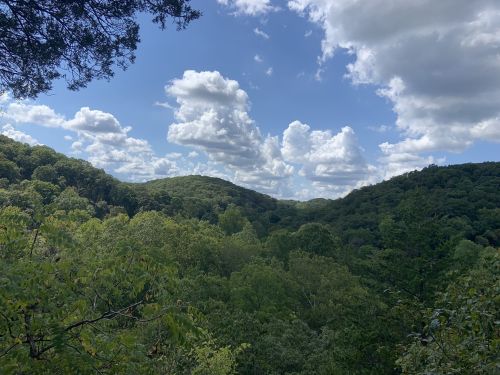 Lush green hills under a blue sky with fluffy clouds, creating a serene natural landscape.