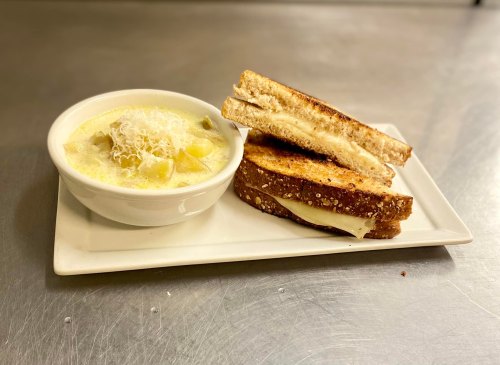 A plate with a bowl of creamy soup and two slices of toasted cheese sandwich.