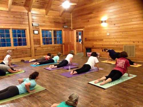 A group of people practicing yoga in a wooden studio, lying on mats in a relaxed position.