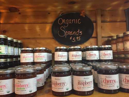 Shelves filled with jars of organic fruit spreads, including strawberry, raspberry, and cherry, priced at $5.95.