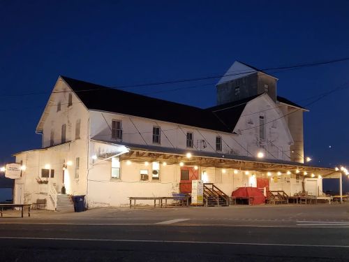 A large, white building with a dark roof, illuminated at night, featuring a porch and outdoor seating.