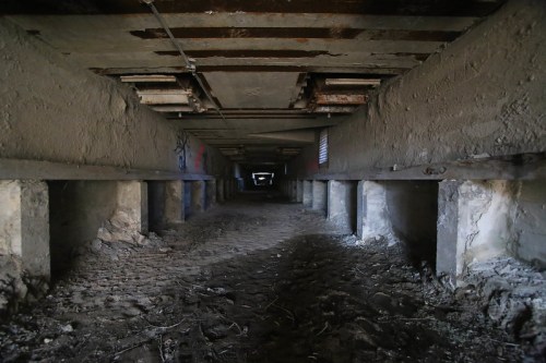 A dimly lit underground passage with rough walls and a dirt floor, supported by concrete pillars.