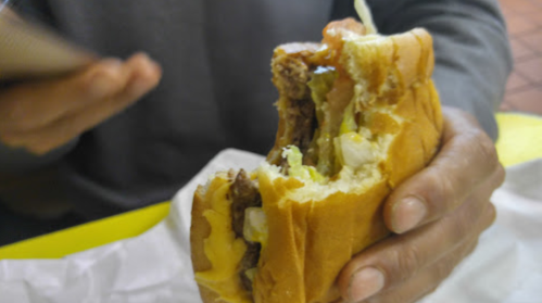 A person holds a partially eaten burger with lettuce, tomato, and cheese, against a blurred background.