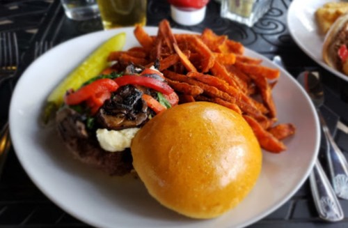 A plate featuring a burger with toppings, a pickle, and a side of sweet potato fries.