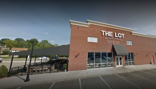 Exterior view of "The Lot," a brick building with a patio and awning, set against a clear blue sky.
