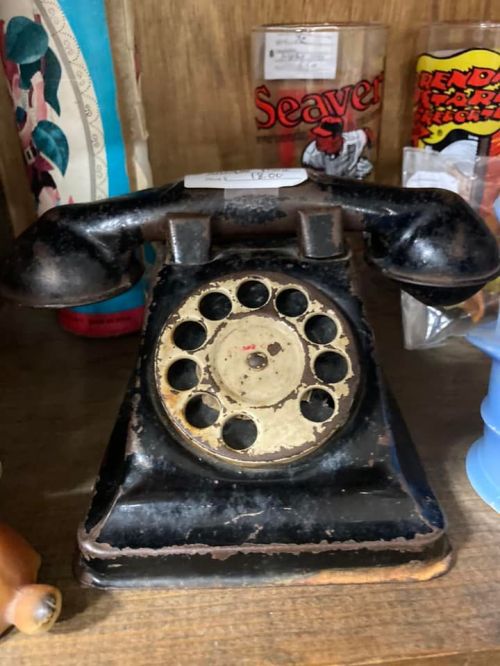 A vintage black rotary phone displayed on a shelf among various collectibles.