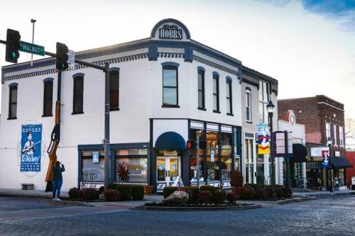 A corner building with a sign reading "Hobbs," featuring storefronts and street signs in a quaint town setting.