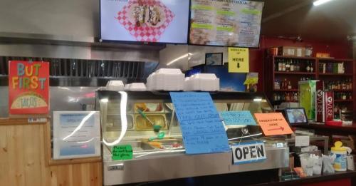 A colorful taco shop interior with a display case, menus on the wall, and signs indicating it's open for business.