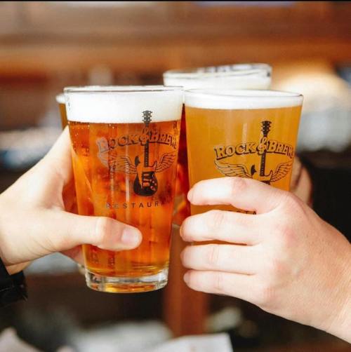 Four glasses of beer are clinking together, featuring the logo of "Rock & Brews" restaurant.