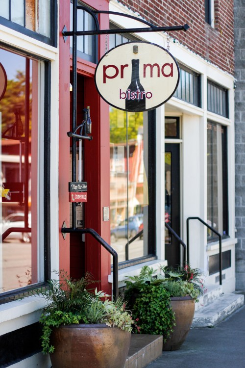 Exterior of Prima Bistro with a sign and planters, showcasing a welcoming entrance on a sunny day.