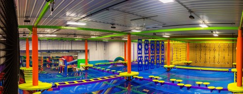 A colorful indoor trampoline park with various play areas, including climbing walls and obstacle courses.