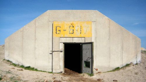 Concrete bunker with a yellow sign labeled "G-017" and a large metal door, set against a clear blue sky.
